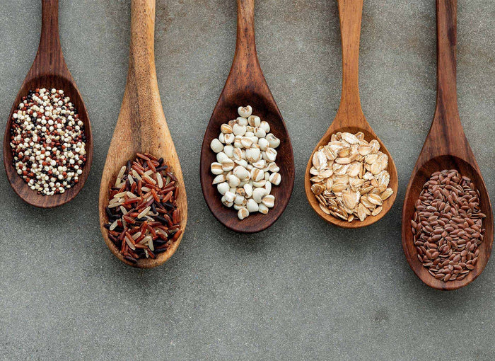 Fünf Holzlöffel mit Quinoa, Wildreis, Hirse, Haferflocken und Leinsamen – ballaststoffreiche Lebensmittel im Vergleich