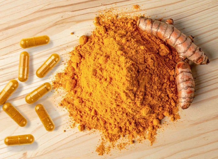 Curcuma-Kapseln neben einem Haufen Curcuma-Pulver und frischen Wurzeln auf Holzuntergrund