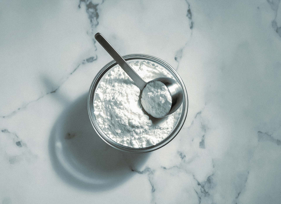 Kreatin-Pulver mit Messlöffel in einem Glas, von oben fotografiert auf Marmoruntergrund