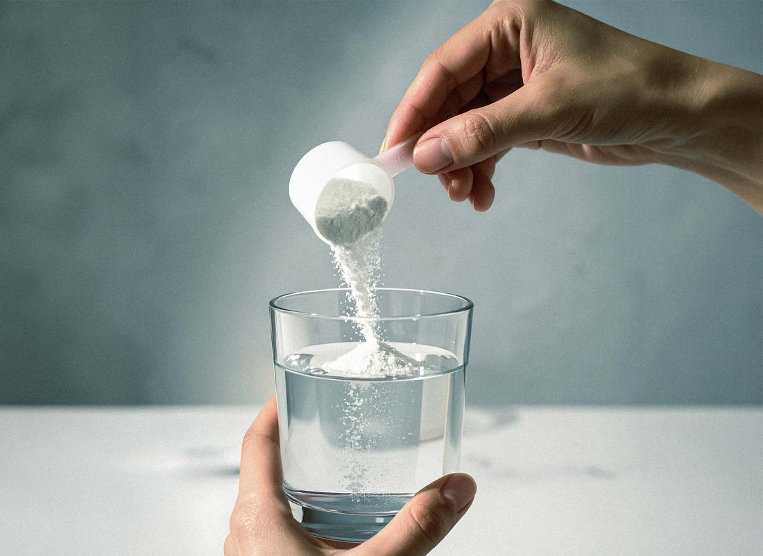 Hand schüttet weißes Pulver aus einem Messlöffel in ein Glas Wasser – Kreatin als gut erforschtes Supplement