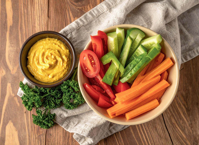 Schüssel mit Gemüsesticks aus Tomate, Gurke, Paprika und Karotte neben einem cremigen Dip – gesunde Ernährung im Alltag