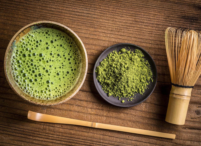 Matcha-Tee mit Bambusbesen und Matcha-Pulver auf einem Holztisch – traditionelle japanische Zubereitung